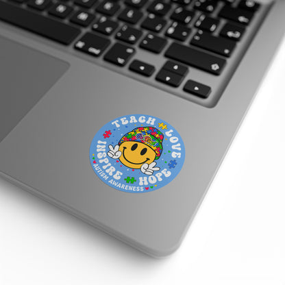 Autism awareness round sticker roll with smiley puzzle piece labels featuring "Teach Love Inspire Hope" message on paper.